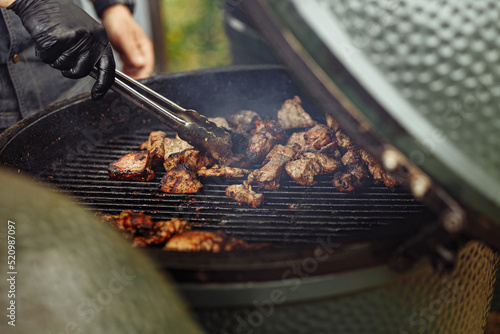 Close up image of The Green Egg outdoor barbecue. Very popular ceramic bbq. A hand of a cook preparing BBQ