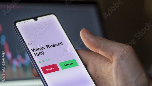 Un investisseur analyse un fonds etf valeur russell 1000 sur un graphique. Un téléphone affiche le cours de l'ETF. Texte en français francais Valeur Russell 1000