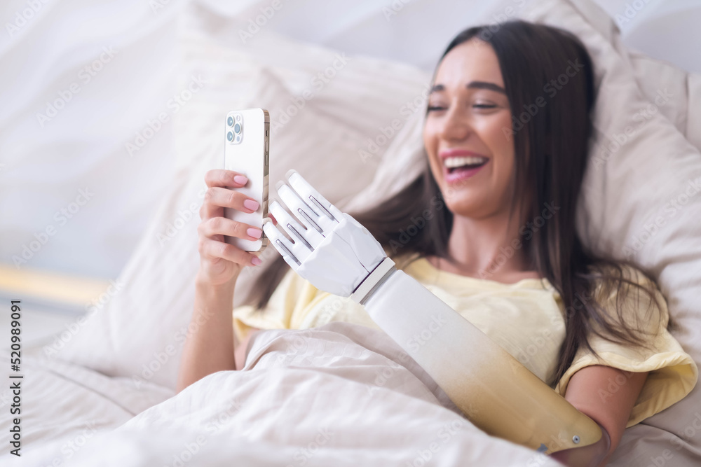 Girl disability bionic arm using phone, reading social media and chatting in bed, disabled cyborg woman leads normal life artificial prosthetic limb, working online remotely from home Girl disability bionic arm using phone, reading social media and chatting in bed, disabled cyborg woman leads normal life artificial prosthetic limb, working online remotely from home