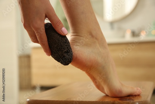 Fotografija Woman using pumice stone for removing dead skin from feet in bathroom, closeup