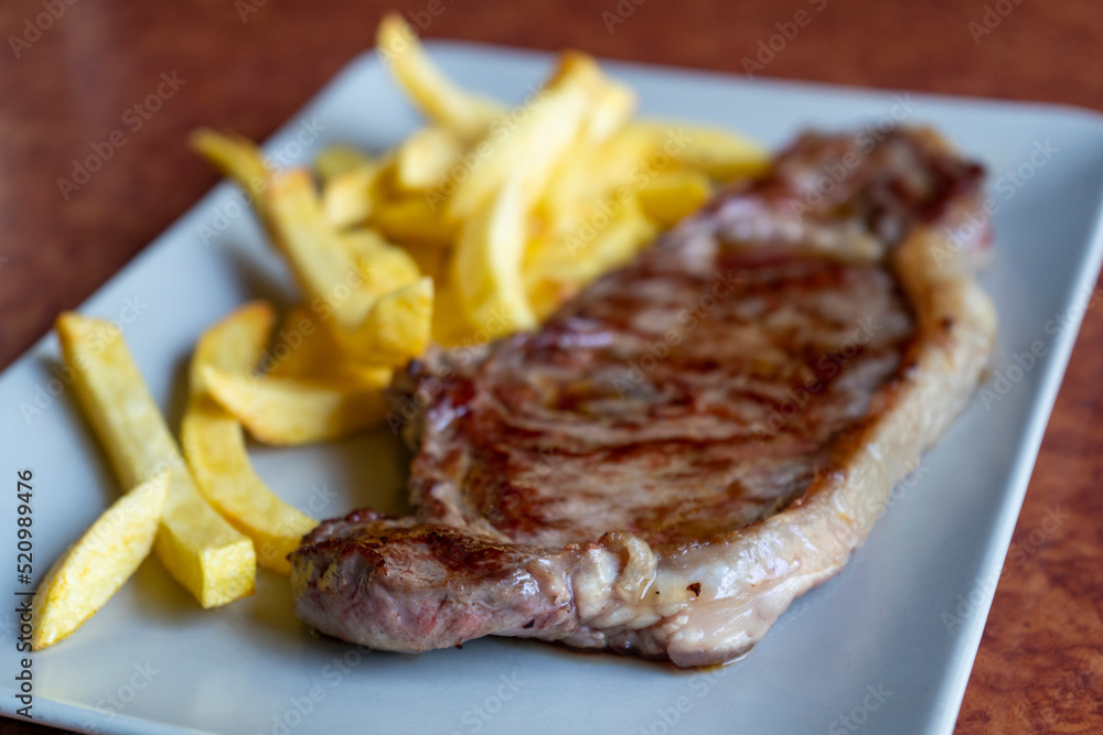 Detalle de Entrecot de ternera con patatas emplatado en un plato blanco