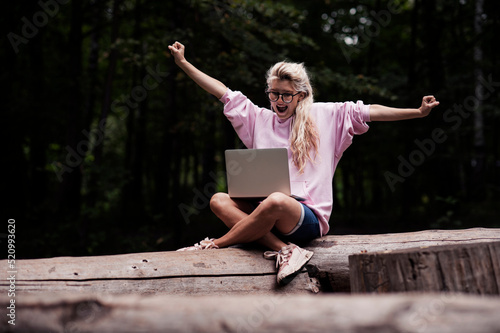 A girl with a laptop works while walking in the park in a cozy place, enjoys it. Online learning, freelancing and fun concept, talk by mobile cell phone look aside. People urban lifestyle concept