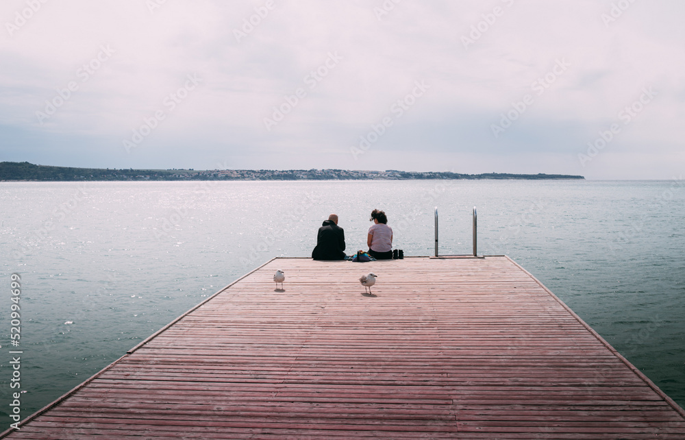 Couple man and woman sitting on sea coast dock watching the horizon