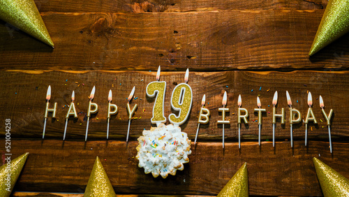 golden letters of the candle with the number happy birthday, the background of the pie with candles happy birthday on the background of brown stranded boards. Postcard Happy birthday 79