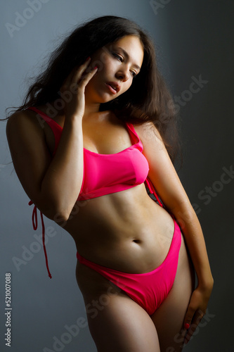 a beautiful Brazilian woman in a pink swimsuit poses on a gray background