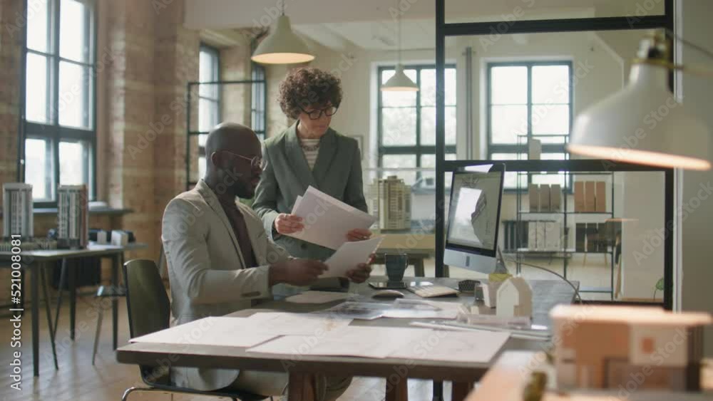 African American man and Caucasian woman discussing architectural project on paper and computer while working together in office African American man and Caucasian woman discussing architectural project on paper and computer while working together in office