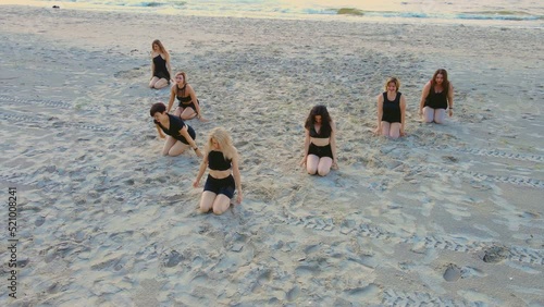 Group of seven athletic women practicing yoga lesson outdoor with instructor at ocean beach at sunset. Healthy active lifestyle and outdoor training concepts photo