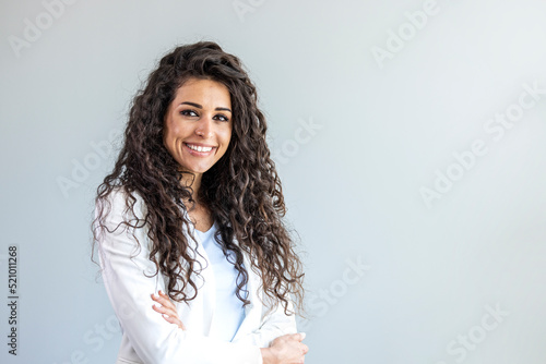 Waist up portrait modern business woman in the office with copy space. Portrait of a happy and confident young woman standing posing against a gray wall. Businesswoman with arms crossed