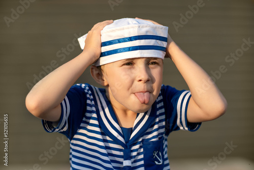 A boy of 7-8 years old in a sailor suit teases and shows his tongue. Close-up portrait of a child.
