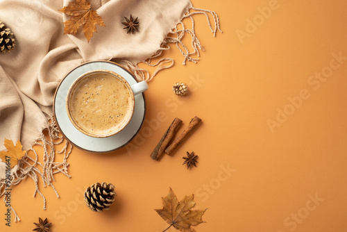 Autumn mood concept. Top view photo of cup of frothy drinking on saucer anise cinnamon sticks yellow maple leaves scarf and pine cones on isolated orange background