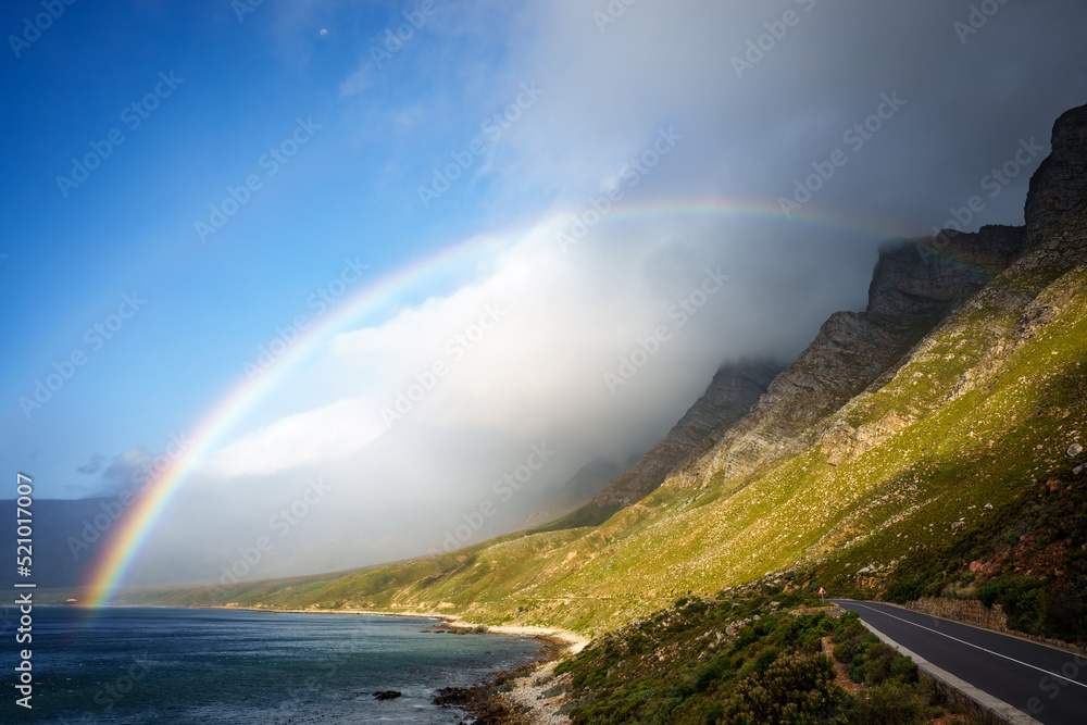 A rainbow and storm over the Kogelberg Mountains along the coastline from Clarence Drive between Gordon's Bay and Rooi-Els on the eastern part of False Bay, Cape Town, Western Cape, South Africa.