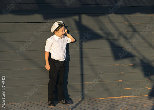 Little ship captain on the deck of a pirate ship. The boy stands on the deck of the ship with a shell in his hands. The boy listens to the sea shell.