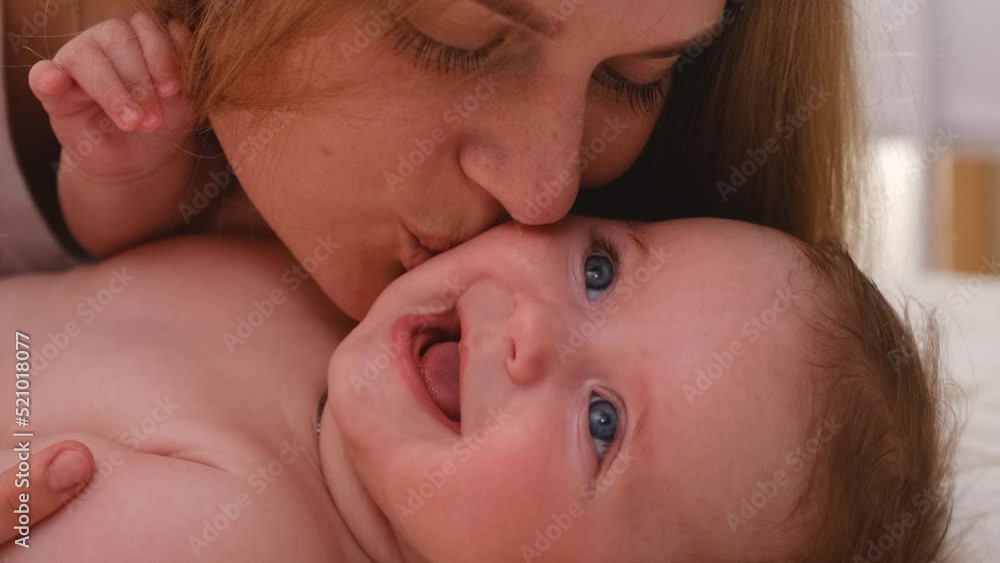 close up Young loving mother with brunette short hair plays with newborn son in grey crawlers tickling and making baby boy smile and laugh loudly closeup. close up Young loving mother with brunette short hair plays with newborn son in grey crawlers tickling and making baby boy smile and laugh loudly closeup.