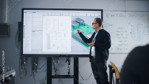 Male Teacher Standing Near Digital Interactive Whiteboard and Talking to Group of Diverse Students About Computer Motherboard Components: Microchips, CPU Processor, Transistors, Semiconductors photo