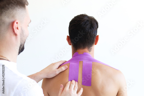 Kinesiology taping. Kinesiology tape on patient neck. Young male athlete on white background. Post traumatic rehabilitation, sport physical therapy, recovery concept, alternative medicine.