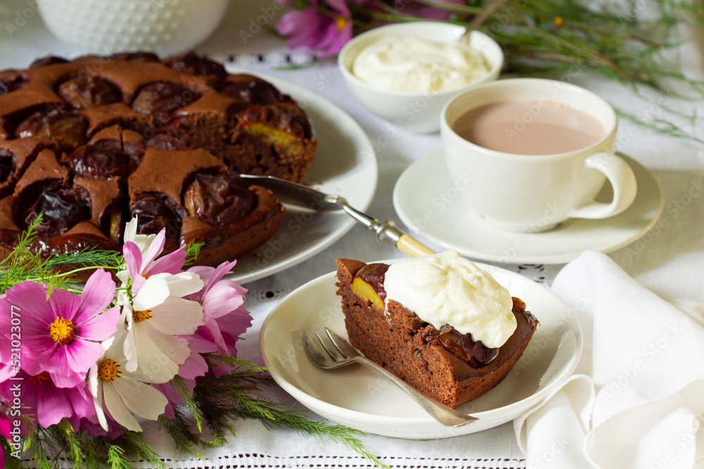 Chocolate plum cake with whipped cream, served with cocoa. Rustic style.