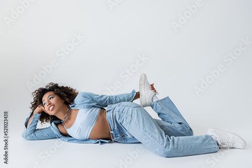 Photo african american woman in trendy denim clothing looking away while lying on grey