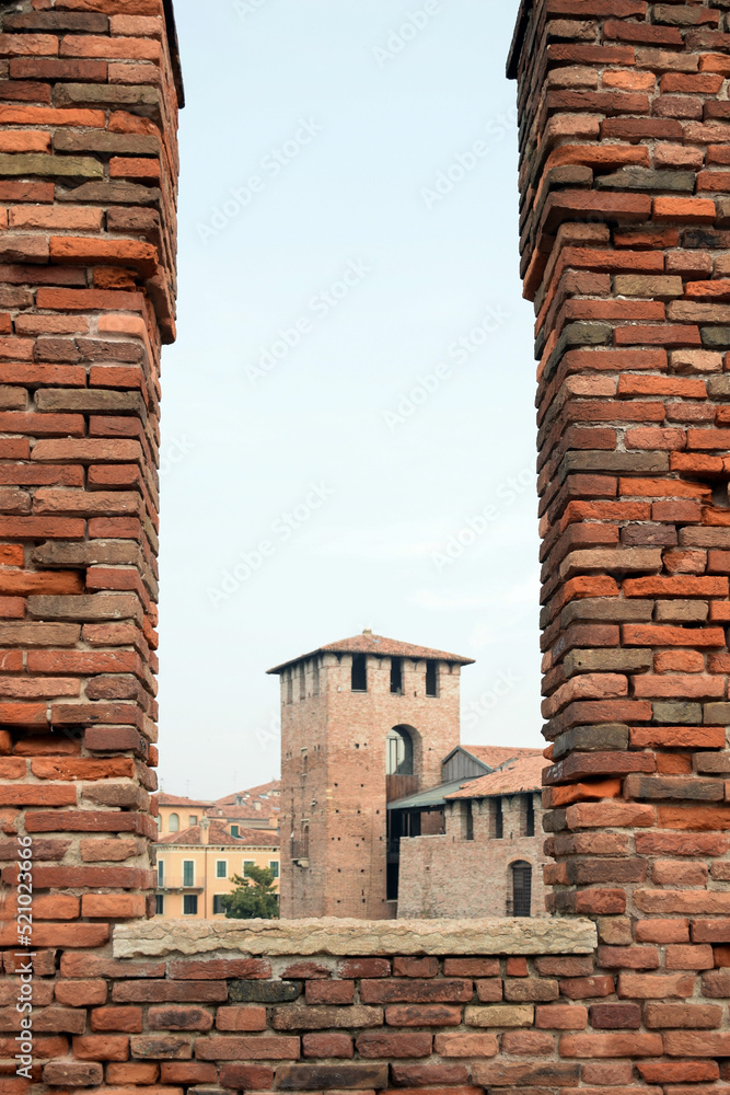 A tower of a medieval fortress through an embrasure opening in a brick wall