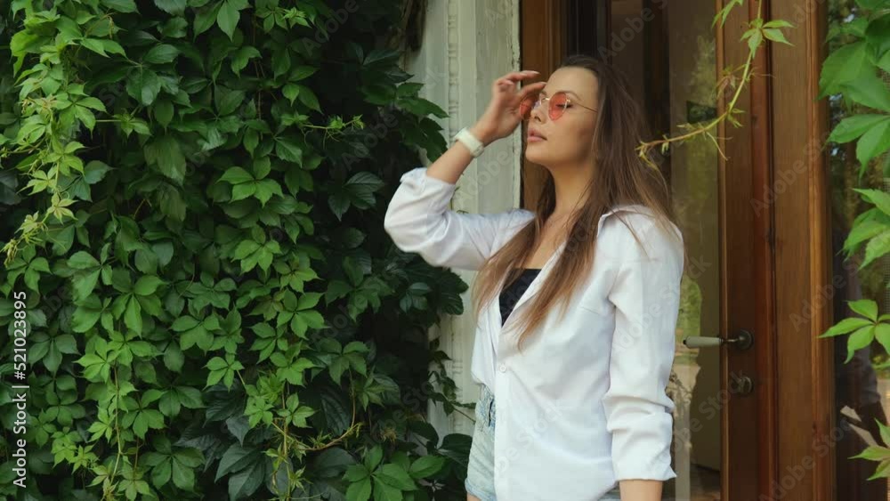 A beautiful young woman in a white shirt stands near the door in nature in green foliage. Slow motion portrait. Woman portrait A beautiful young woman in a white shirt stands near the door in nature in green foliage. Slow motion portrait. Woman portrait