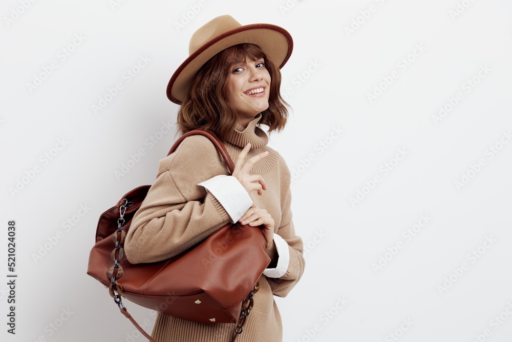 a happy woman stands on a white background on the floor sideways in a sweater, shirt and hat, holding a bag on one shoulder, looking away in surprise a happy woman stands on a white background on the floor sideways in a sweater, shirt and hat, holding a bag on one shoulder, looking away in surprise