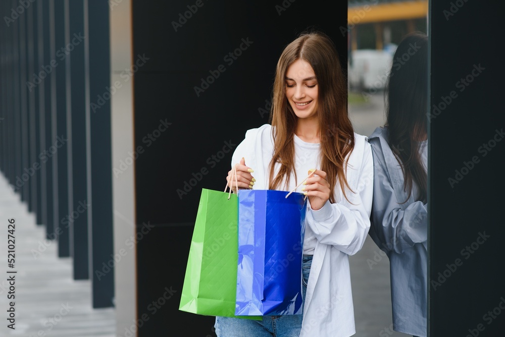 Fashionable beautiful happy woman standing with shopping bags near a shopping center on Black Friday. Fashionable beautiful happy woman standing with shopping bags near a shopping center on Black Friday.