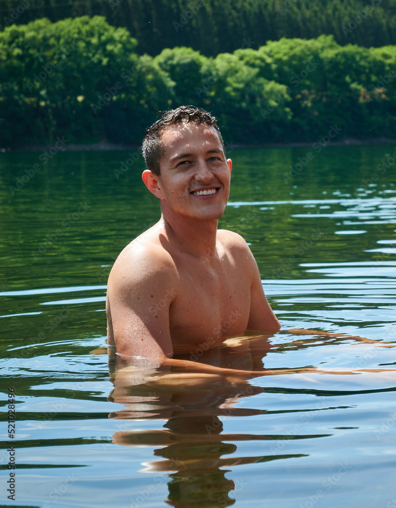 Fototapeta premium A vertical shot of a smiling man in the lake looking at the camera against a forest