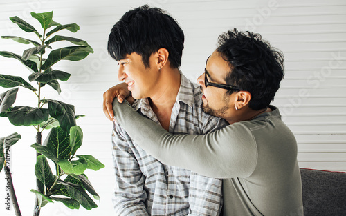 Portrait Gay LGBT sweet Asian couple wearing pajamas, hugging with happiness and love, reconcile partner while getting sulk, sitting in cozy living room at home, cute posing in Lifestyle Concept. photo