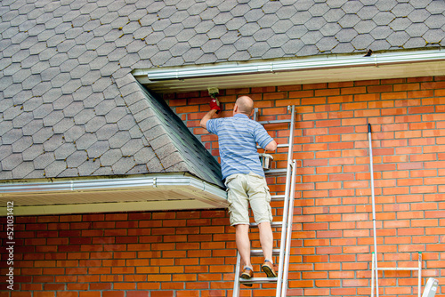 Man home owner working repainting house with paint brush and white paint outdoors in summer. photo