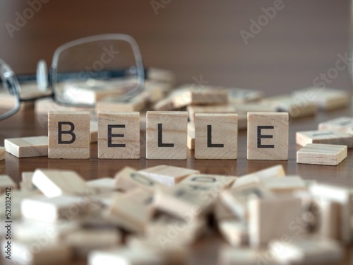 belle word or concept represented by wooden letter tiles on a wooden table with glasses and a book photo