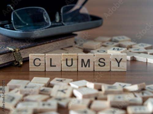 clumsy word or concept represented by wooden letter tiles on a wooden table with glasses and a book photo