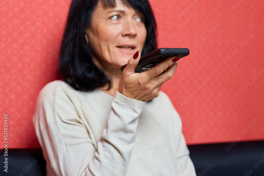 Senior woman sit on sofa speak to microphone dictate audio message on smartphone Senior woman sit on sofa speak to microphone dictate audio message on smartphone