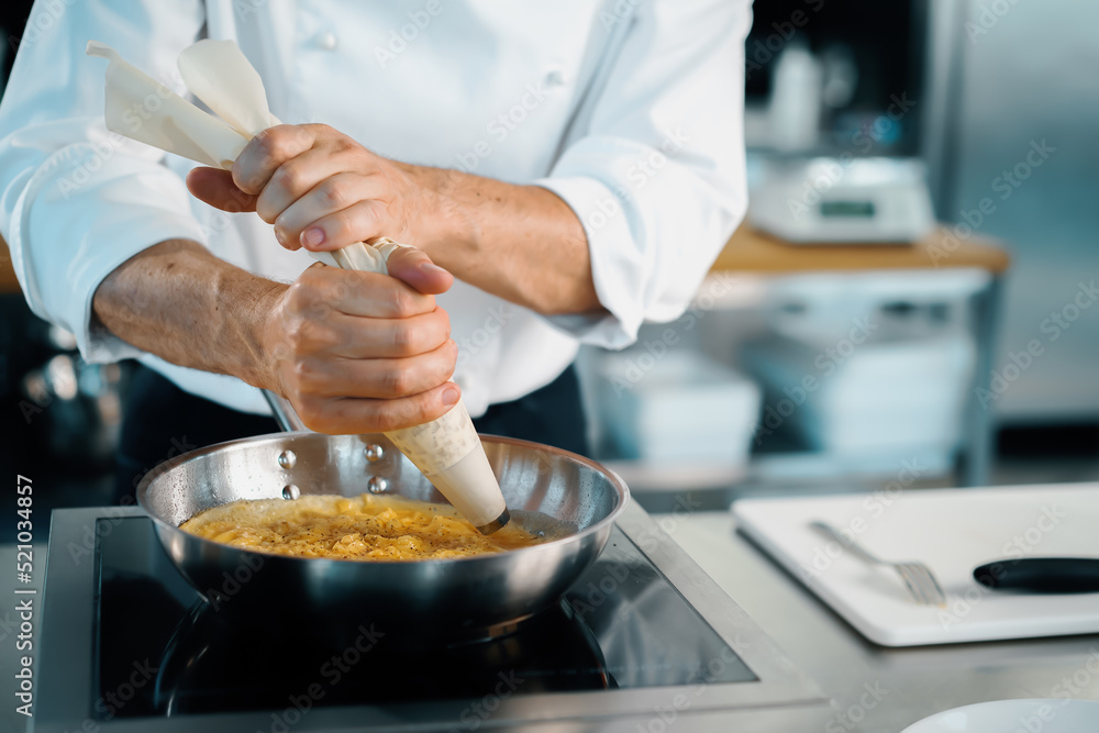Professional kitchen of a restaurant, close-up: a male chef prepares a french omelette in a frying pan