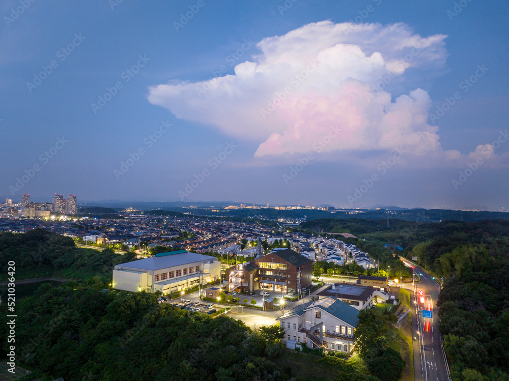 Lone towering cloud over bright buildings and suburban development at dusk