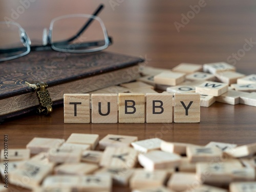 tubby word or concept represented by wooden letter tiles on a wooden table with glasses and a book photo