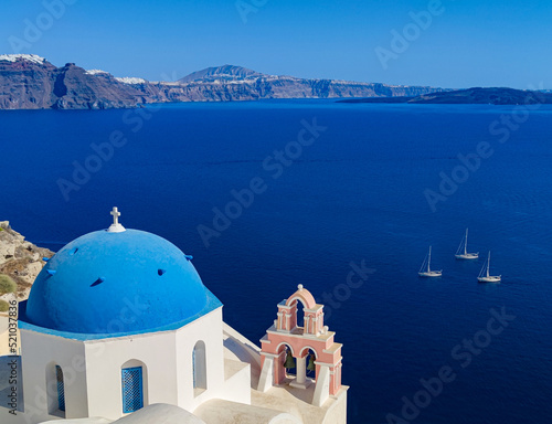 photography of point view from OIA village in santorini island, greece to the caldera volcano with some boats and blue and white churches