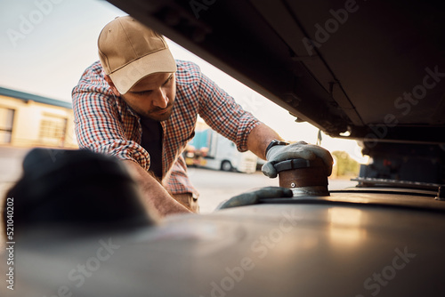 Professional truck driver checking gas tank on parking lot. photo