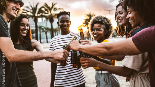 Happy multiracial friends toasting beer bottles together outside - Group of young people having beach party on summer vacation - Youth lifestyle concept