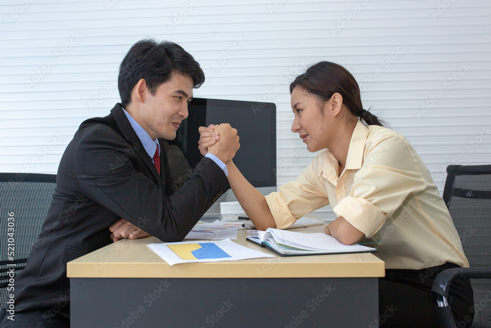 Asian business man and business women doing arm wrestling on desk in office and they challenge face to face Asian business man and business women doing arm wrestling on desk in office and they challenge face to face