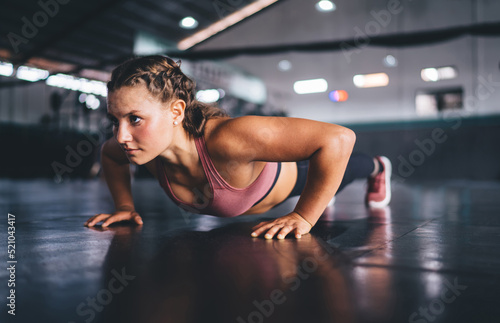 Determined female training during pushing up exercises activity and healthy lifestyle, muscular fit girl practice plank exercises toning physical strength during cardio workout in sportive gym