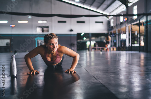 Strong Caucasian female athlete doing push ups having workout for warming up muscles, determined fit girl reaching fitness goals exercising in gym studio training body and physical strength