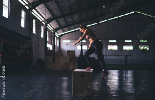 Good looking female athlete in tracksuit workout on equipment box during training time in sportive gym studio, Caucaisan fit girl slimming and exercising for keeping figure and body shape in tonus