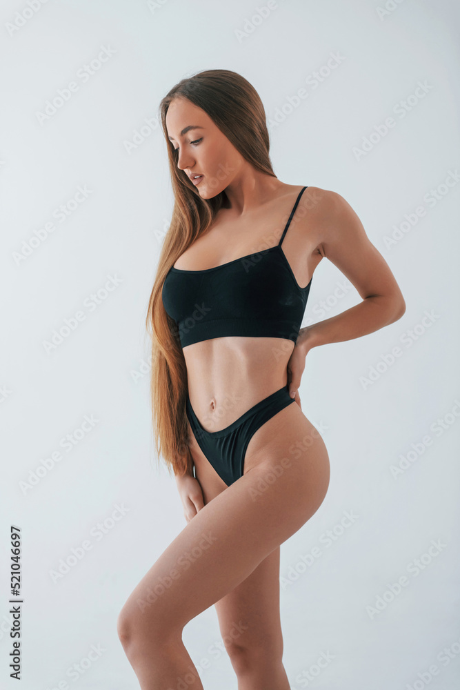 Fototapeta premium Standing in black lingerie. Woman in underwear with slim body type is posing in the studio