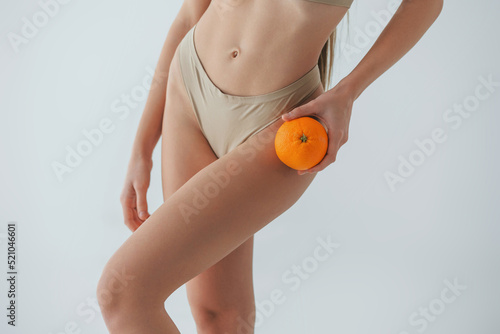 Holding orange fruit. Woman in underwear with slim body type is posing in the studio