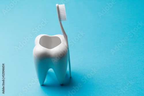 The concept of dental health and dental care. Day of the dentist. A white toothbrush leaned on a white tooth on a blue background. Healthy tooth. Place for text. Close-up
