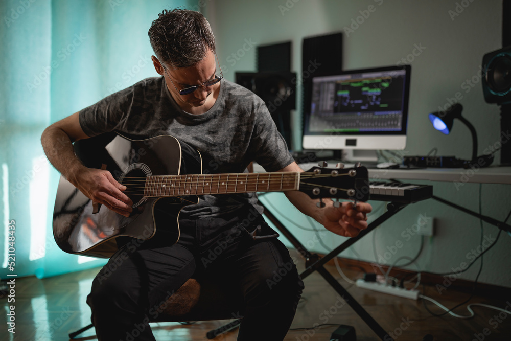 Obraz premium Guitarist and producer tuning his acoustic guitar before recording some parts for a project at his home studio