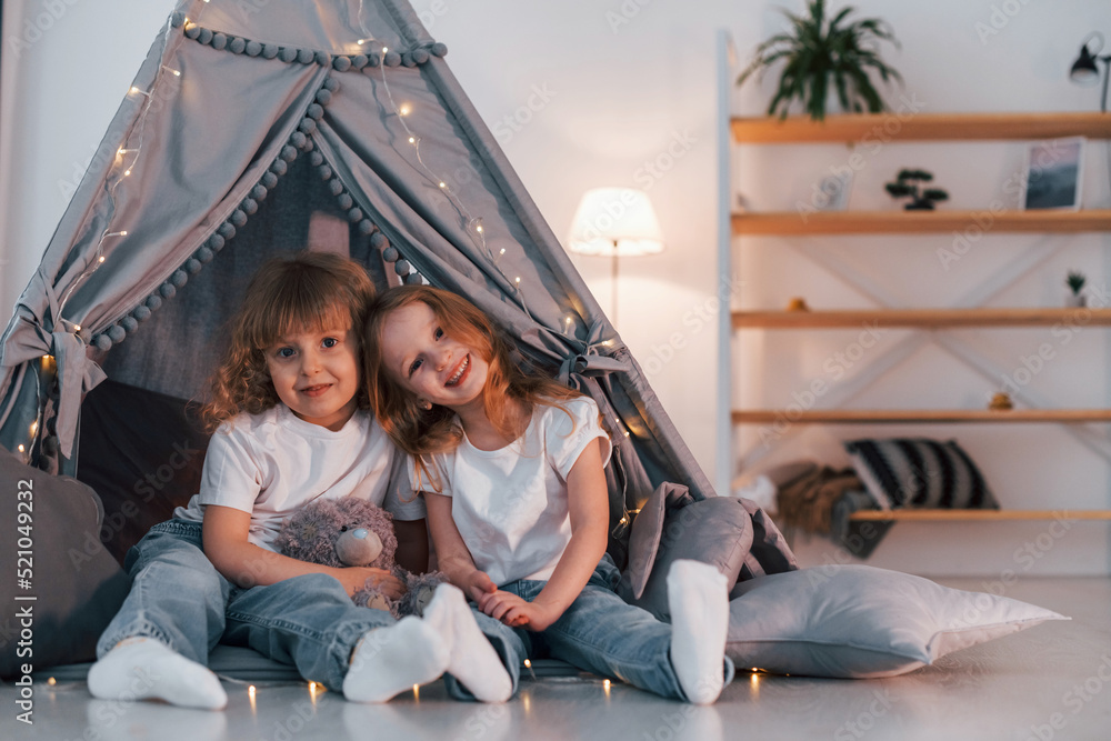 Embracing each other. Two little girls is in the tent in domestic room together Embracing each other. Two little girls is in the tent in domestic room together