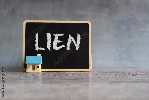 Toy house and chalkboard with text LIEN. Property and real estate concept photo