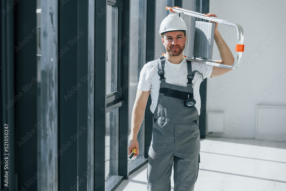 Holding ladder. Repairman is working indoors in the modern room Holding ladder. Repairman is working indoors in the modern room