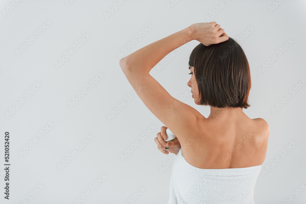 Using ball deodorant. Young brunette is indoors against white background Using ball deodorant. Young brunette is indoors against white background