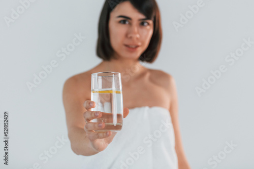 Holding glass with water. Young brunette is indoors against white background
